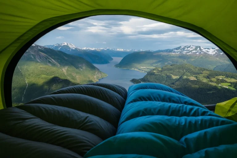View from inside a tent overlooking mountains and a lake, with a sleeping bag in the foreground.